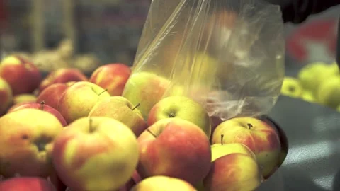 The young man customer puts the fresh apples in a disposable plastic bag. Stock Footage 131554713