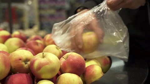 The young man customer puts the fresh apples in a disposable plastic bag. Stock Footage 131554836