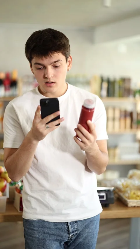 Young man customer at shop scans QR code on smoothie package using phone camera Stock Footage 315025538