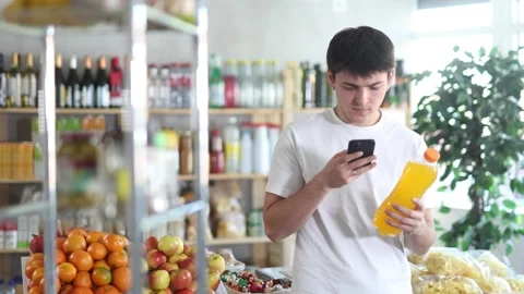 Young man customer at shop scans QR code on drink bottle using phone camera Stock Footage 317530434