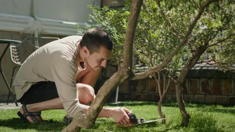 Young man cuts carefully grass with scissors in yard smiling Stock Footage 217856602