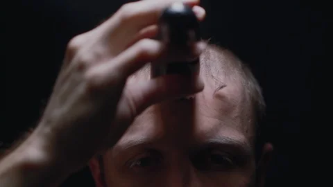 Young man is cuts himself using a clipper in a dark room in front to camera. Stock Footage 128120509