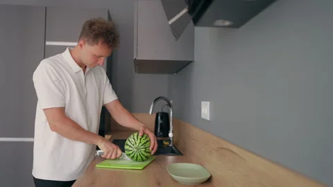 Young Man Cutting a Fresh Watermelon on a Cutting Board in the Kitchen Stock Footage 340109003