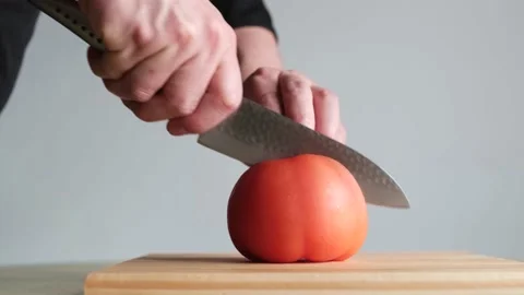 Young man cutting a ripe red tomato into four segments on a wooden board Stock Footage 133808728