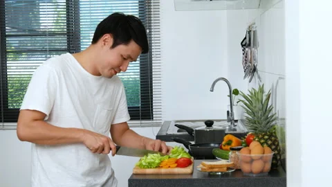 Young man cutting vegetables for preparing healthy food in the kitchen at home Stock Footage 170708539
