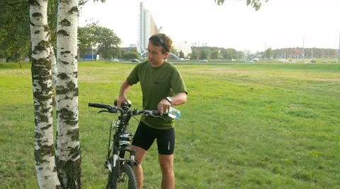 A young man cyclist stops and drink water from bottle. Against the background of Stock Footage 66453021