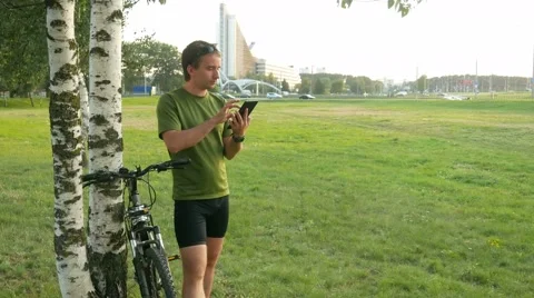 A young man cyclist touch tablet near the birch . Against the background of Stock Footage 66453452