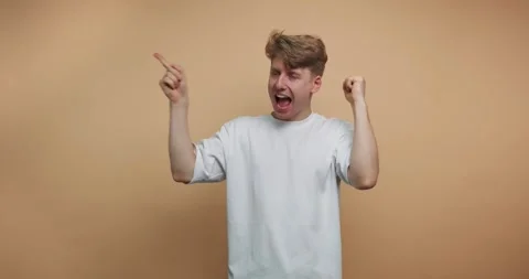 Young man dances happily and gestures in front of a plain orange background Stock Footage 328247101