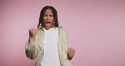 Young man dances joyfully in front of a pink background during a fun event .. Stockbeeldmateriaal 326787982