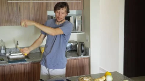 A young man dances joyfully while cooking in the kitchen. A lively and cheerful Stock Footage 320473068