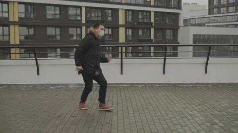 A young man dances walking along a fence against a backdrop of high houses Stock Footage 136744405