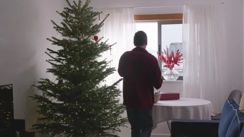 Young man dancing and decorating Christmas tree in cozy bright living room, 4K. Stock Footage 324923901