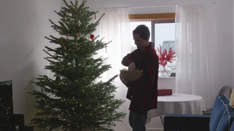 Young man dancing and decorating Christmas tree in cozy bright living room, 4K. Stock Footage 324923994