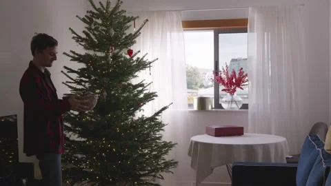 Young man dancing and decorating Christmas tree in cozy bright living room, 4K. Stock Footage 324924050