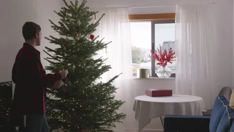 Young man dancing and decorating Christmas tree in cozy bright living room, 4K. Stock Footage 324924090
