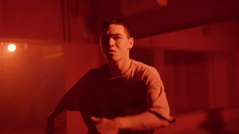 Young man dancing contemporary hip hop on red neon background in studio wearing Stock Footage 253576806