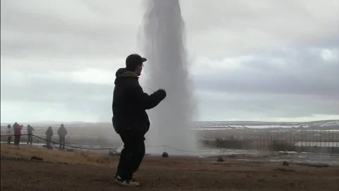 Young man dancing funny in front of erupting geysir in Iceland Stock Footage 259720165