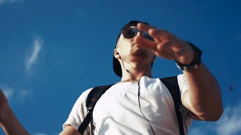 Young man dancing with headphones on the sky background Video stock 94974933