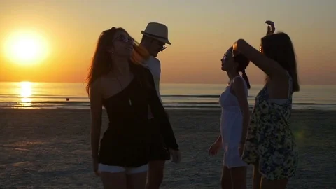 Young man dancing with three female friends on the shore of the ocean at tw.. Stock Footage 71385313