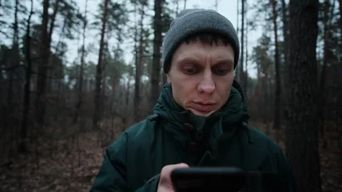 A young man in a dark green jacket, lost in the forest at dusk, walks into focus Stock Footage 300951351