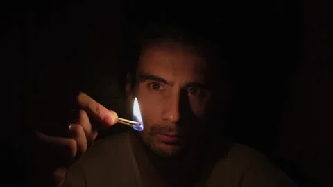 A young man in the dark lights the matches and lights up his face Stock Footage 153235995