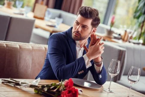 Young man on date in restaurant sitting with bouquet nervous Stock Photos