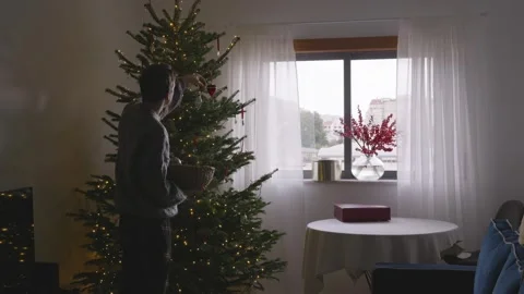Young man decorating Christmas tree in cozy bright living room Stock Footage 324923763
