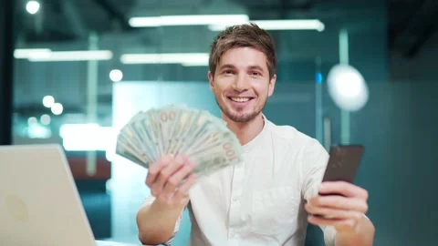 Young man developer holding fan of cash money dollar banknotes sitting at work Stock Footage 229095743