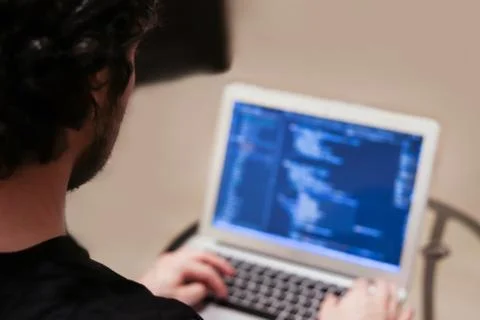 Young man is developing complex software on laptop on blurred background. Vie Stock Photos