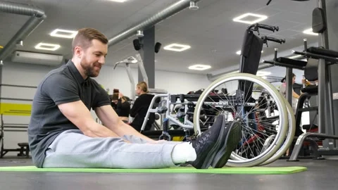 A young man with disabilities does mobility exercises in the gym. Video stock 222459639