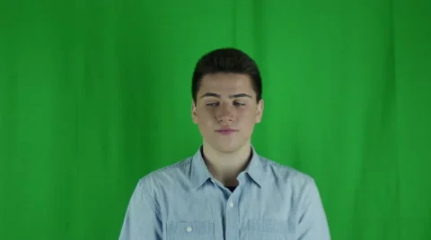 Young man is dismissive in front of a greenscreen in a blue shirt Vidéo 59085421