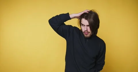 Young man displays a playful expression while contemplating, on yellow back.. Stock Footage 314336986