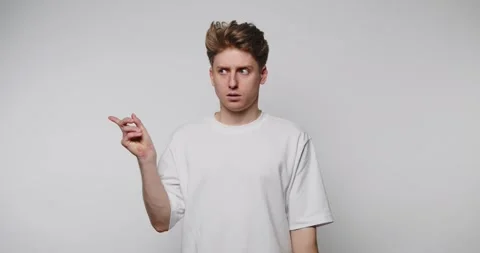 A young man displays a surprised expression while pointing in a minimalisti.. Stock Footage 316180847