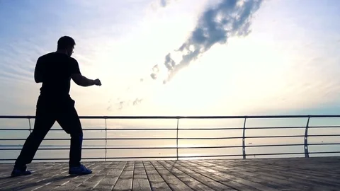 Young man does round house high kicks barefooted against sunrise in slow motion Video stock 77725191