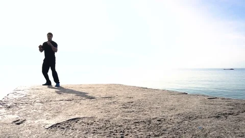 Young man does round house high kicks barefooted against sunrise in slow motion Stock Footage 77784894