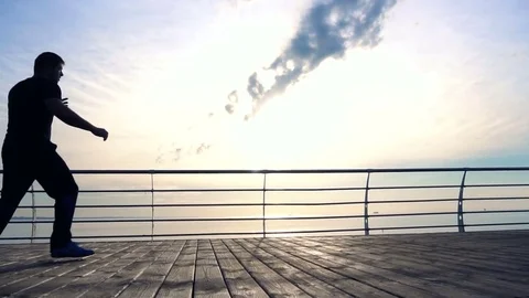 Young man does round house high kicks barefooted against sunrise in slow motion Stock Footage 77785681