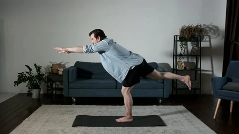 A young Man Does Yoga exercises Stability Balance on One Leg at Home Stock Footage 144238948