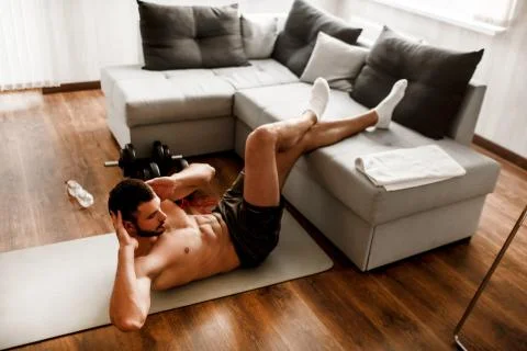 Young man doing abs exercising at home on the couch. Cut view of hardwoking t Stock Photos