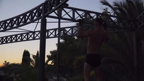 A young man doing back exercises outdoors with a sunset Stock Footage 250935360