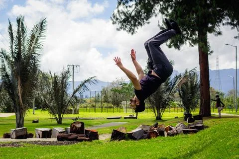 Young man doing a back flip in a park, practicing gymnastics outdoors Stock Photos