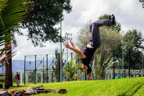 Young man doing a back flip in a park, practicing gymnastics outdoors Stock Photos
