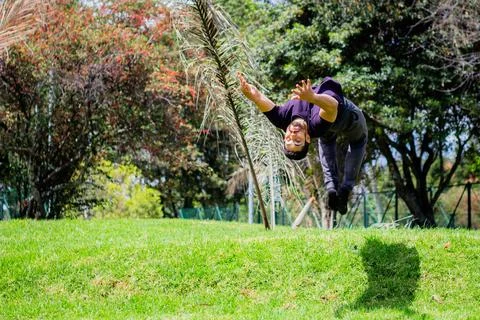 Young man doing a back flip in a park, practicing gymnastics outdoors Stock Photos
