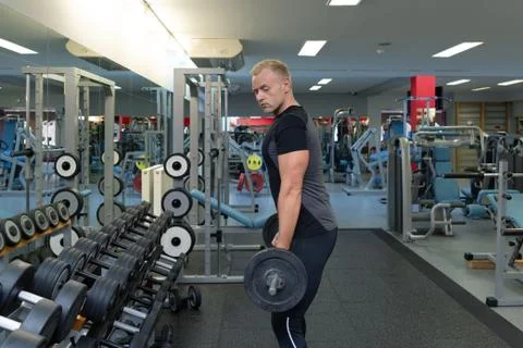 Young man doing the exercises on biceps lifting barbell for good body in fitn Stock Photos