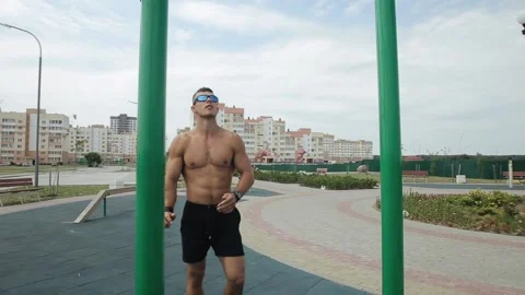 Young man doing exercises on the city sports field and pulling up on the Видео 138498760