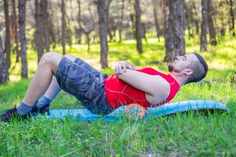 Young man doing exercises with a foam roller outdoor, free space. Stock Photos