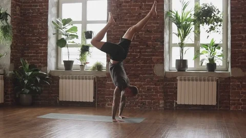 Young man doing hand standing pose. Guy doing yoga indoors near windows 스톡 동영상 107103812