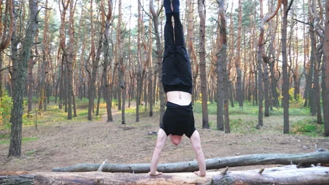 Young man doing handstand on log in fore... | Stock Video | Pond5