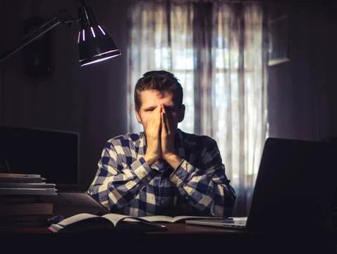 Young man doing home task with lots of books and laptop under the lamp Stock Photos