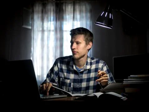 Young man doing home task with lots of books and laptop under the lamp Stock Photos