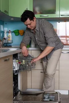 Young man doing homework in the kitchen. Puts the dishes in the dishwasher fo Stock Photos